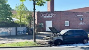 Vor einem Club steht ein ausgebrannter Pkw auf einer Straße. © Screenshot 