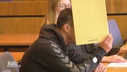 Eine Person hält sich im Gerichtssaal einen Aktenordner vors Gesicht. © Screenshot 
