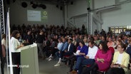 Mitglieder der Grünen sitzen beim Sonderparteitag in einer großen Halle. © Screenshot 
