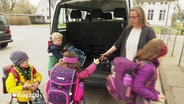 Grundschulkinder werden aus einem Kleinbus verabschiedet. © Screenshot 