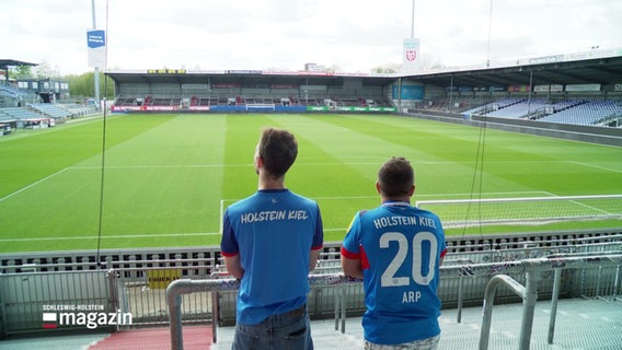 Zwei Personen in Trikots blicken ins Stadion von Holstein-Kiel. © Screenshot 