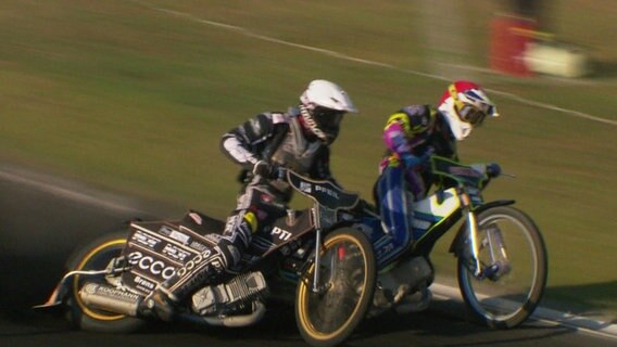 Zwei Motorradfahrer fahren um eine Kurve bei einem Speedway-Rennen in Stralsund. © Screenshot 