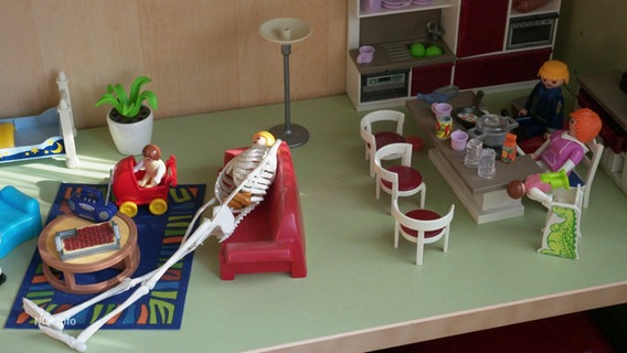 Spielfiguren sind in einem Puppenhaus platziert. © Screenshot 
