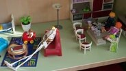 Spielfiguren sind in einem Puppenhaus platziert. © Screenshot 