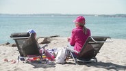 Eine Frau und ein Kind sitzen in Liegestühlen am Strand. © Screenshot 