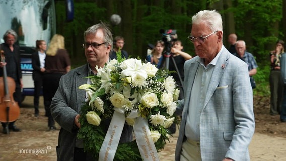 Zwei Männer tragen einen weißen Blumenkranz. © Screenshot 