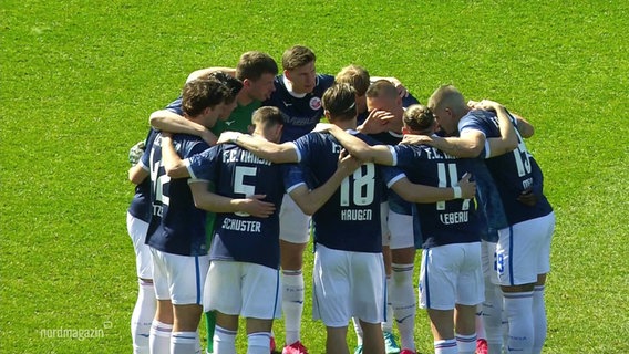 Die Spieler von Hansa Rostock stehen im Kreis und fassen sich an den Schultern. © Screenshot 