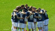 Die Spieler von Hansa Rostock stehen im Kreis und fassen sich an den Schultern. © Screenshot 