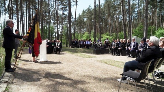 Viele Menschen sitzen im Wald im Kreis vor einem Rednerpult. © Screenshot 