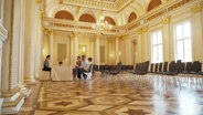 Ein Paar wird in einem großen goldenen Saal getraut. © Screenshot 