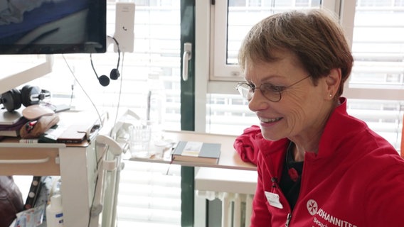 Ein Frau in einer roten Jacke in einem Krankenhauszimmer. © Screenshot 