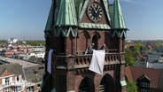 Weiße Lacken hängen an allen Seiten des Kirchturms in Elmshorn, um an die Aktion "Weiße Flagge" zum Kriegsende 1945 zu gedenken. © Screenshot 