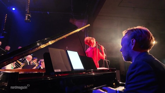 Ein Mann spielt Klavier auf einer Bühne. Im Hintergrund singt die dänische Jazz-Musikerin Sinne Eeg. © Screenshot 