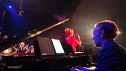 Ein Mann spielt Klavier auf einer Bühne. Im Hintergrund singt die dänische Jazz-Musikerin Sinne Eeg. © Screenshot 