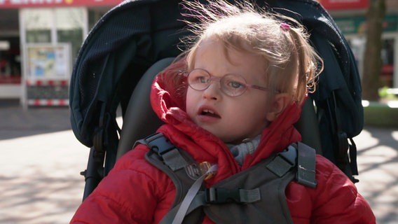 Ein Mädchen sitzt in einem Kinderwagen. © Screenshot 