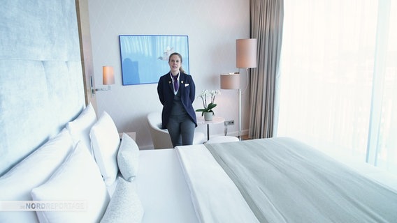Eine Hotelangestellte steht neben einem großen Hotelbett © Screenshot 