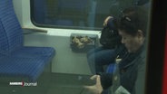 Blick durch die Scheibe einer S-Bahn auf einen offenen und übervollen Müllbehälter zwischen den Sitzen. © Screenshot 