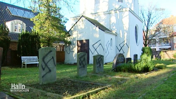 Eine Kirche und mehrere Grabsteine sind mit Hakenkreuzen beschmiert. © Screenshot 