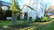 Eine Kirche und mehrere Grabsteine sind mit Hakenkreuzen beschmiert. © Screenshot 