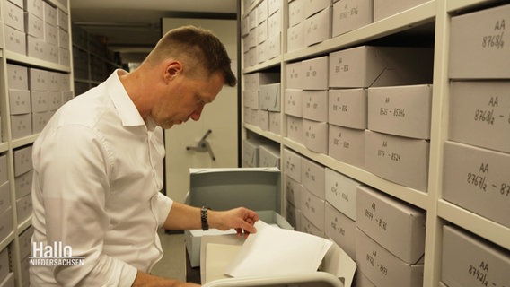 Ein Archivar steht an einem Aktenschrank und blättert in Unterlagen. © Screenshot 