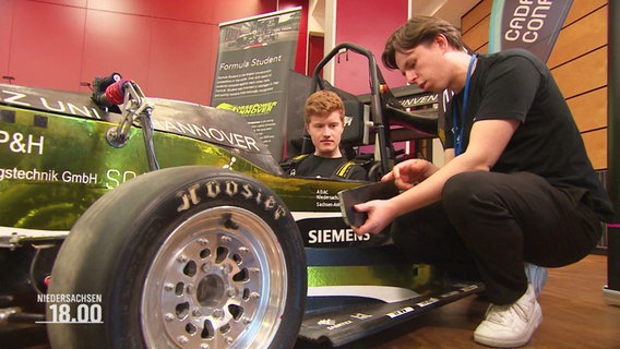 Zwei Studenten hocken neben demPrototypen eines elektrischen Rennwagens. © Screenshot 