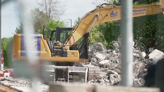 Blick durch einen Bauzaun auf einen Bagger auf einer Baustelle © Screenshot 