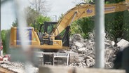 Blick durch einen Bauzaun auf einen Bagger auf einer Baustelle © Screenshot 