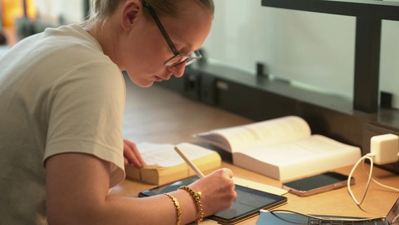 Eine Studentin sitzt an einem Tisch und macht Notizen auf einem Tablet. © Screenshot 