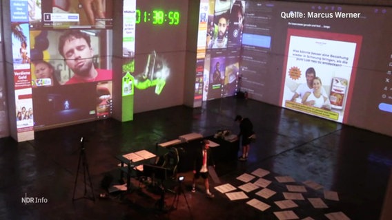 Die Bühne bei einem Theaterstück mit digitalen Monitoren im Hintergrund und an der Seite. © Screenshot 