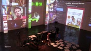 Die Bühne bei einem Theaterstück mit digitalen Monitoren im Hintergrund und an der Seite. © Screenshot 