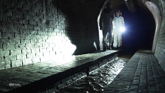 Menschen in Schutzanzügen laufen durch einen unterirdischen Tunnel. © Screenshot 