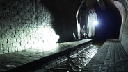 Menschen in Schutzanzügen laufen durch einen unterirdischen Tunnel. © Screenshot 