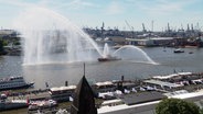 Ein Blick auf die Elbe mit mehreren Schiffen, eines davon spritz Wasserfontänen in unterschiedliche Richtungen. © Screenshot 