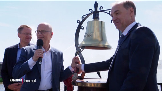 Peter Tschentscer und zwei weitere Männer stehen an einer großen Glocke. © Screenshot 