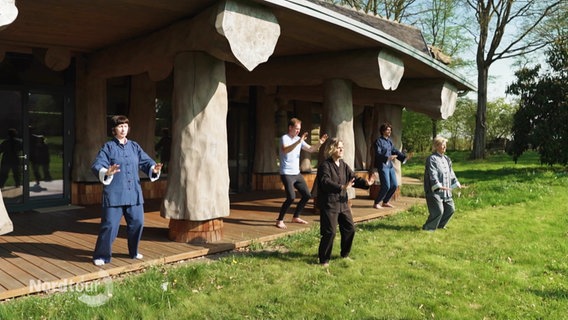 Fünf Frauen und Männer praktizieren im Garten Tai Chi. © Screenshot 