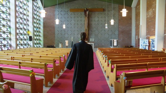 Ein Pastorin läuft in einen leeren Kirchenraum. © Screenshot 