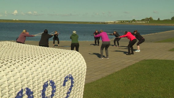 Gruppe von Frauen bei einer Übung mit Walkingstöcken am Wasser. © Screenshot 