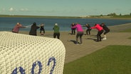 Gruppe von Frauen bei einer Übung mit Walkingstöcken am Wasser. © Screenshot 