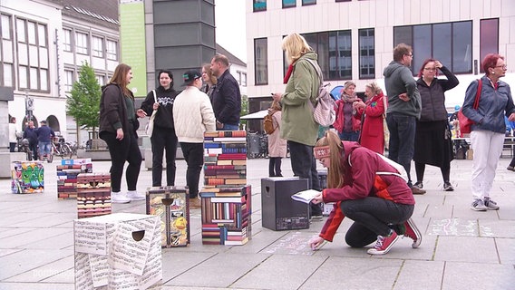 Ein Marktplatz gefüllt mit Menschen und Büchern. © Screenshot 