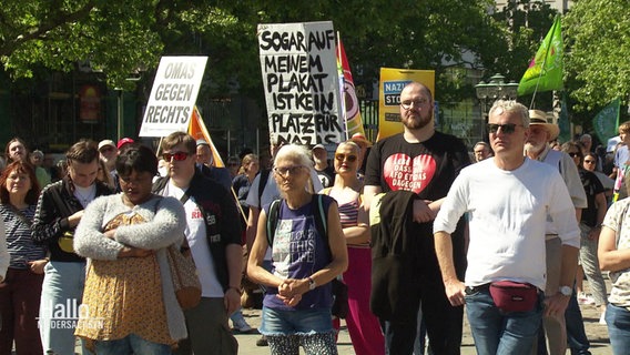 Mehrere Menschen haben sich in bunten Farben und mit Plakaten bei einer Kundgebung gegen die AfD auf einem Platz versammelt. © Screenshot 