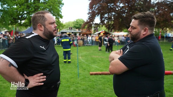 NDR-Reporter Jan Bockemüller steht dem Highland-Games-Sportler Marcel Ende auf einer Rasenfläche gegenüber. © Screenshot 