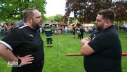 NDR-Reporter Jan Bockemüller steht dem Highland-Games-Sportler Marcel Ende auf einer Rasenfläche gegenüber. © Screenshot 