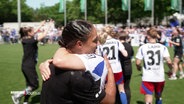 Fußballerinnnen umarmen sich auf einem Spielfeld. © Screenshot 