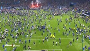 Fans auf dem Spielfeld in einem Stadion. © Screenshot 