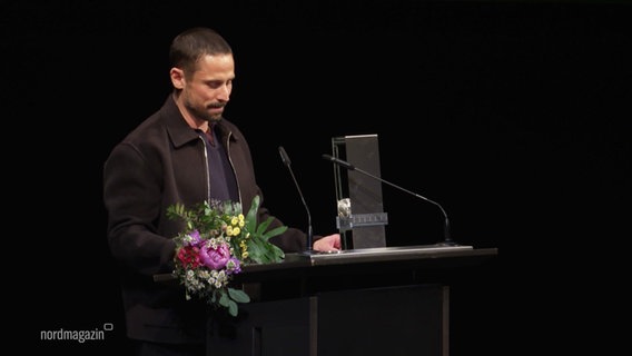 Ein Mann steht bei einer Preisverleihung an einem Rednerpult. © Screenshot 