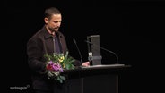 Ein Mann steht bei einer Preisverleihung an einem Rednerpult. © Screenshot 