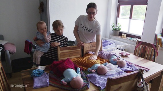 Eine junge Mutter hat ihre drei neugeborenen Drillinge auf dem Küchentisch liegen, neben ihr steht ihre älteste Tochter und hält ein weiteres kleines Geschwisterkind auf dem Arm. © Screenshot 
