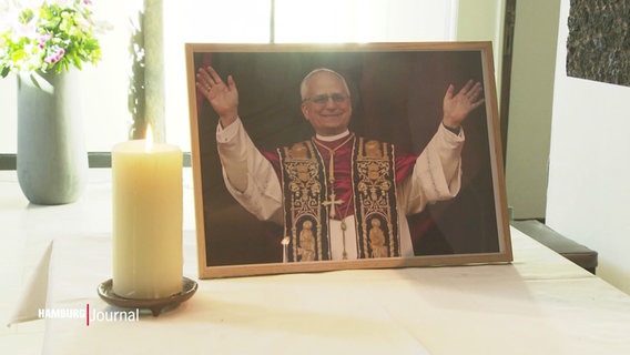 Eine weiße Stumpenkerze und ein gerahmtes Foto von dem frisch gewählten neuen Papst, Leo XIV. © Screenshot 