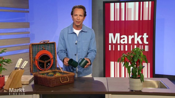 Moderator Jo Hiller im Studio von "Markt". Vor ihm auf dem Tisch ein Picknickkorb mit Kunststoff-Tellern und -Bechern sowie eine Pflanze und ein Messerblock. © Screenshot 