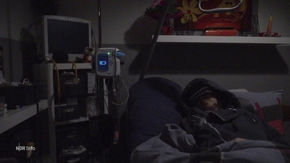 Eine von ME/CFS betroffene Patientin, die nur im Dunkeln liegen kann. Um ihr Bett sind Geräte wie im Krankenhaus zu sehen. © Screenshot 
